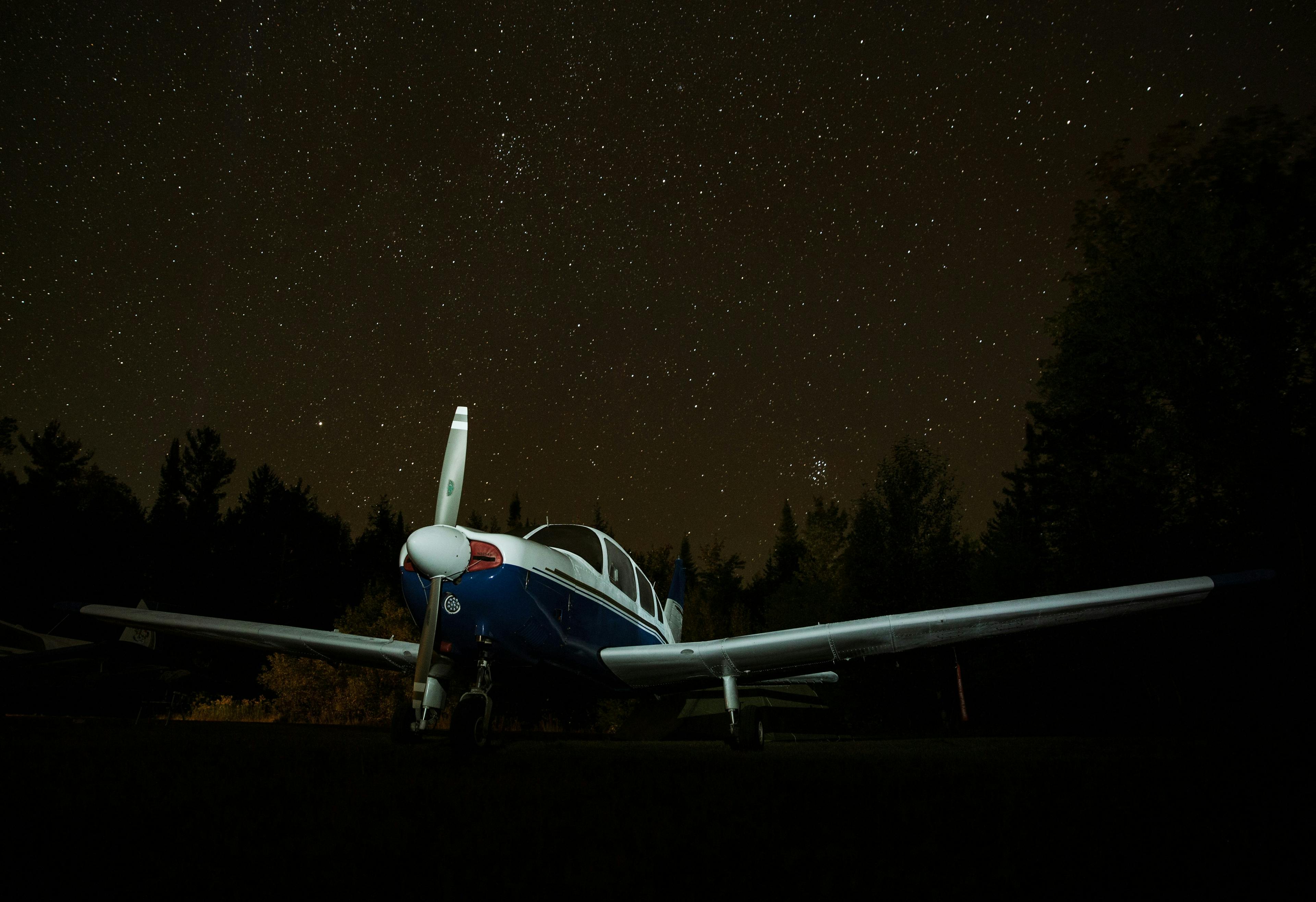 An aeroplane parked under a starry night sky with a couple trees behind it (Photo by Kristina Delp on Unsplash)